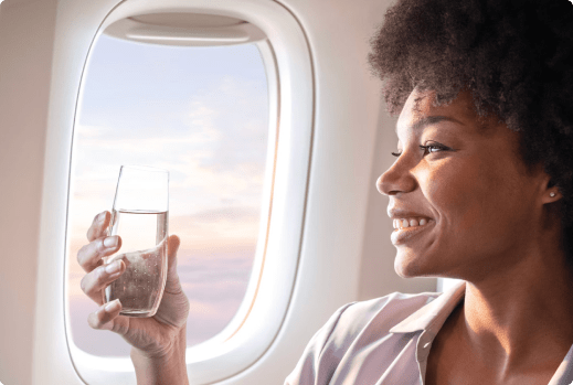 Woman holding a glass of water sitting in the window seat on an airplane